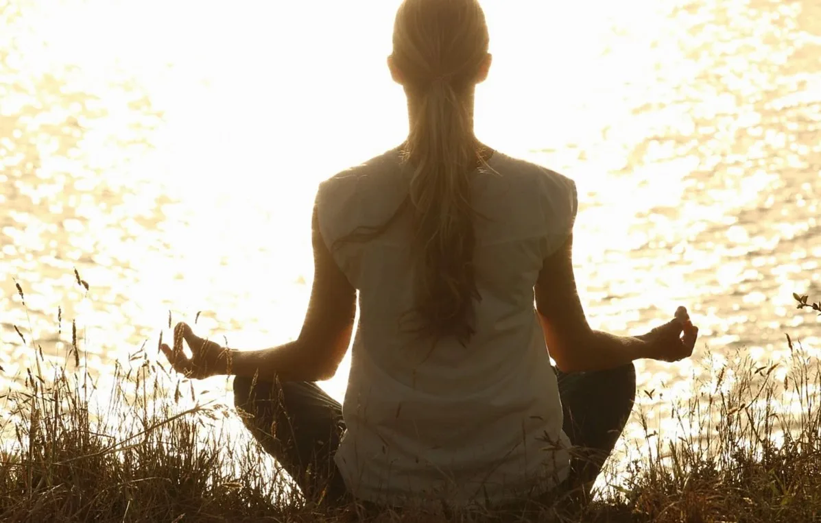 Silhouette of a woman sitting cross-legged in front of sunlit water