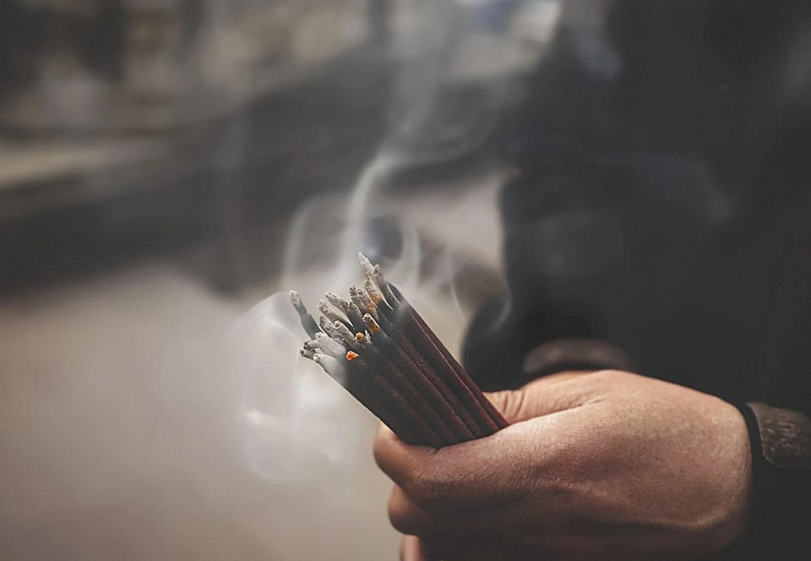 Hand holding a bundle of burning incense sticks with smoke rising