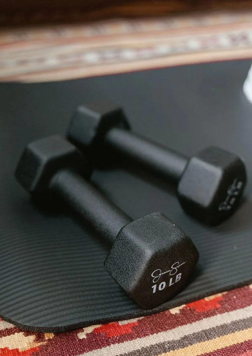 Pair of black dumbbells resting on a dark yoga mat