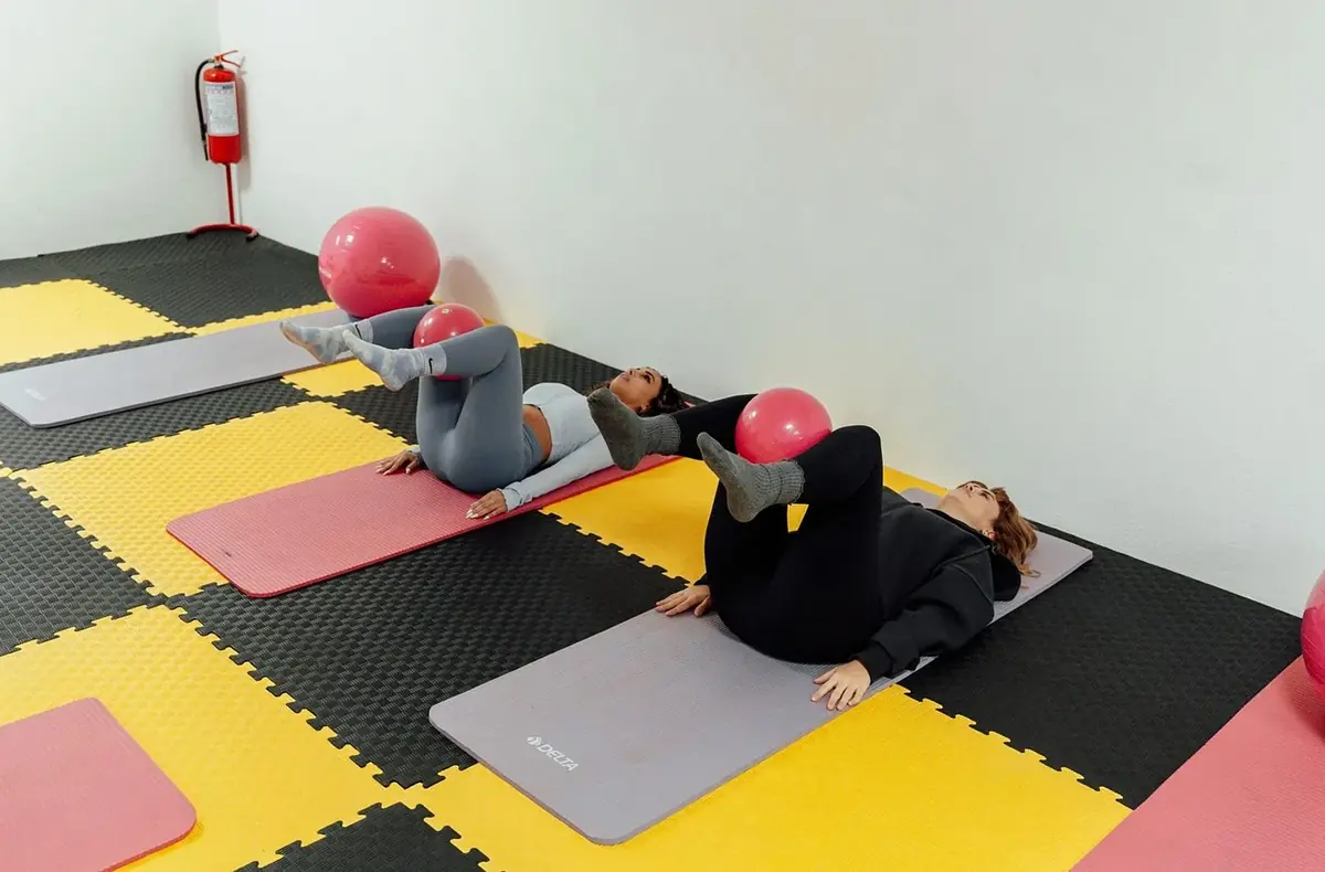 Students lying on mats on a foam-tiled studio floor with small red balls